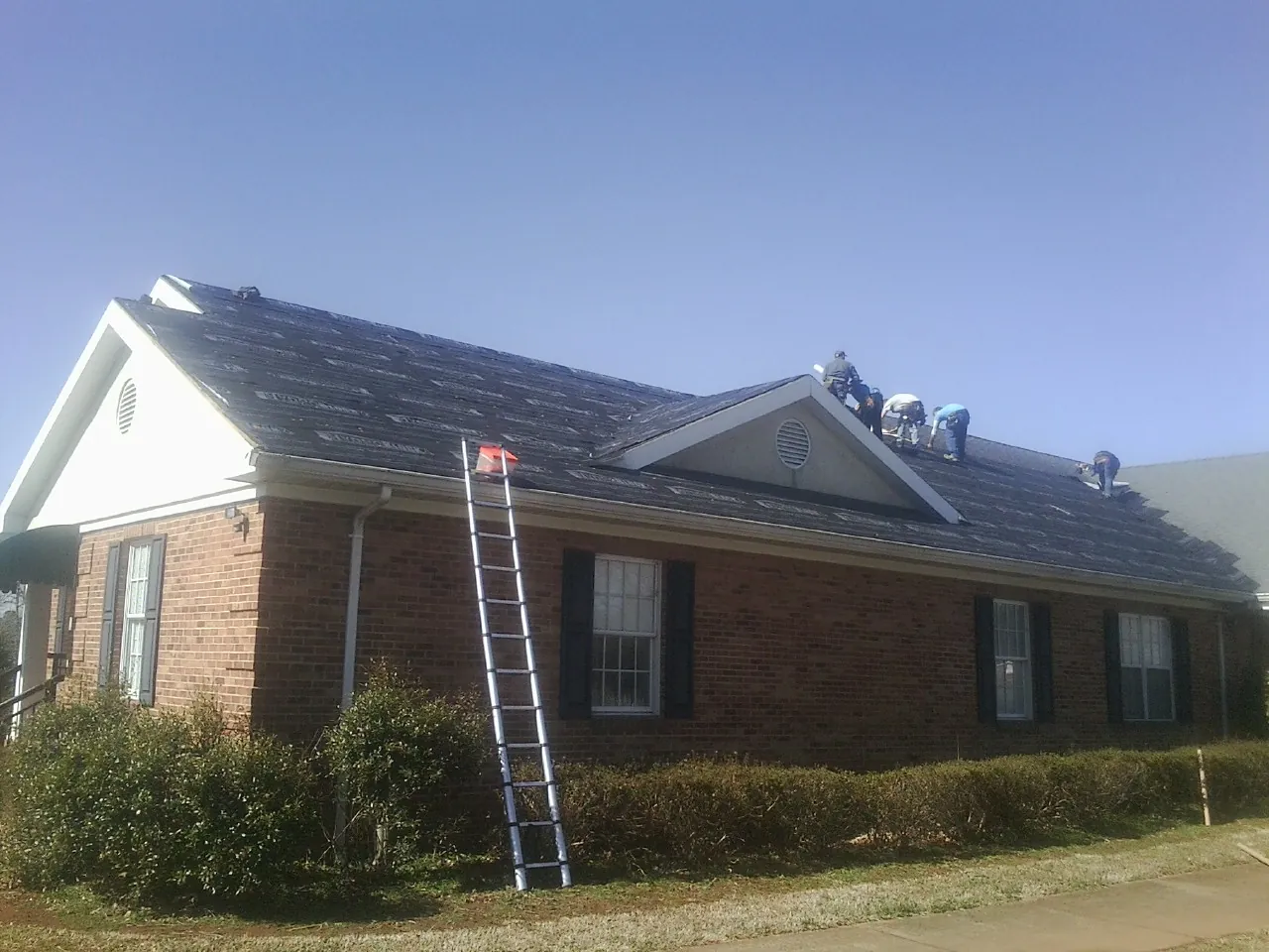 Crew tearing shingles off a brick ranch roof with a ladder set — Metal Roof Repair work by our crew in Clayville