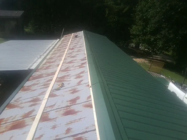 Old rusted panels beside newly installed green metal roofing — Wind Damage Roof Repair by Roofing Brothers in Clayville