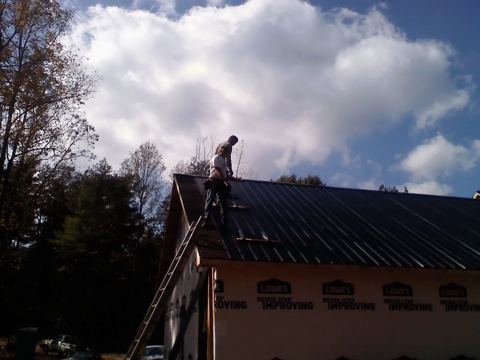 Roofer fastening dark metal panels high against a cloudy sky, from a Roof Inspection job in Clayville
